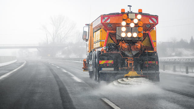 Snow plow salting street in winter time. Orange truck deicing. 